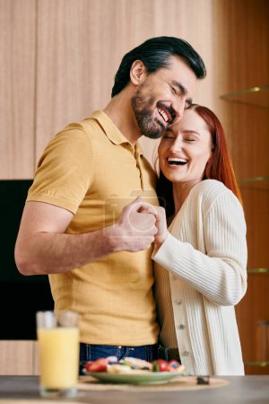 A redhead woman and bearded man stand in their modern kitchen, enjoying quality time together while preparing a meal.
