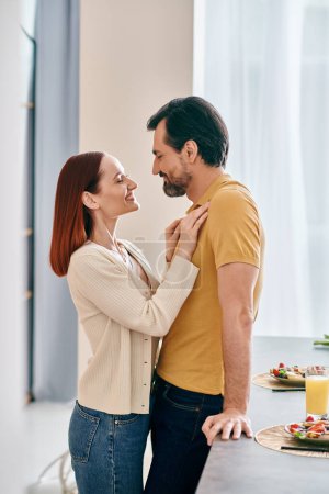 A bearded man and a redhead woman embrace in a warm kitchen, enjoying a moment of togetherness in their modern apartment.