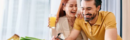 Photo for A redhead woman and bearded man enjoying a glass of orange juice at a table in a modern apartment. - Royalty Free Image