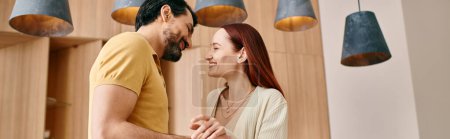 Photo for A redhead woman and bearded man stand in front of a wall in a modern apartment, spending quality time together at home. - Royalty Free Image