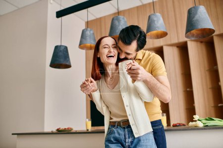 A redhead woman and bearded man gracefully dance in their modern kitchen, enjoying a moment of connection and joy.