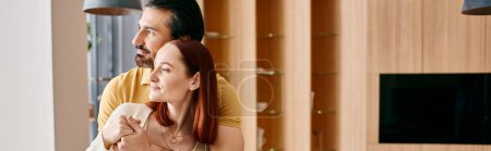 Téléchargez les photos : Un homme barbu et une femme rousse serrent affectueusement dans leur salon élégant, rayonnant de chaleur et d'amour. - en image libre de droit