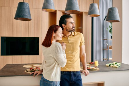 A red-haired woman and bearded man stand together in a stylish kitchen, enjoying a moment of togetherness in their modern apartment.