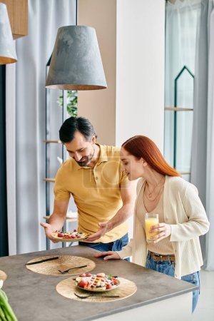 Foto de Una pelirroja y un barbudo disfrutando de una comida juntos en una moderna cocina de apartamentos. - Imagen libre de derechos
