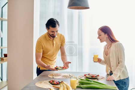 Una hermosa pareja adulta - una mujer pelirroja y un hombre barbudo - compartiendo un plato de comida en una cocina moderna.