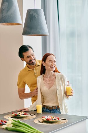 Photo for A redhead woman and a bearded man are enjoying breakfast together in their modern kitchen. - Royalty Free Image