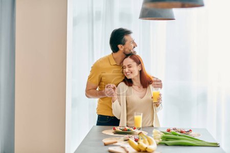 Téléchargez les photos : Une rousse et un barbu prennent le petit déjeuner ensemble dans une cuisine moderne, partageant un moment de connexion et d'amour. - en image libre de droit