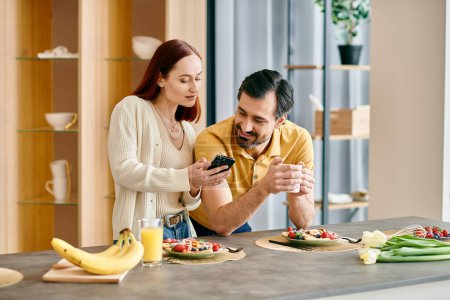Foto de Una hermosa pareja de adultos, una mujer pelirroja y un hombre barbudo, disfrutan de una comida juntos mientras están comprometidos con sus teléfonos. - Imagen libre de derechos