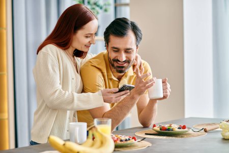 A redhead woman and bearded man are focused on their phones while enjoying breakfast together in a modern apartment.