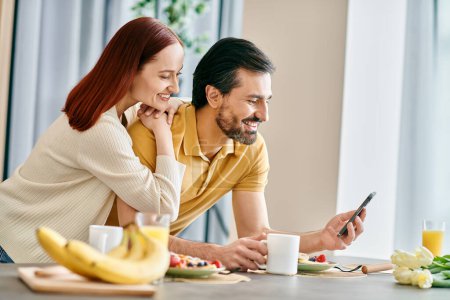 Téléchargez les photos : A beautiful adult couple, redhead woman, and a bearded man, sit at a table engrossed in their phones, enjoying quality time together at home. - en image libre de droit