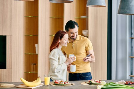 A redhead woman and bearded man gaze at their phone, standing in a modern kitchen, enjoying quality time at home.