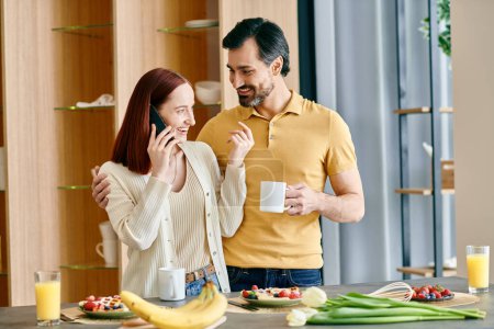Téléchargez les photos : Une rousse et un homme barbu parlent au téléphone tout en prenant le petit déjeuner dans une cuisine moderne. - en image libre de droit