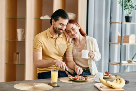 Foto de Una pelirroja y un barbudo están sentados en una mesa de la cocina, desayunando juntos en un apartamento moderno. - Imagen libre de derechos