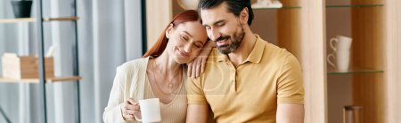 Photo for A beautiful adult couple, a redhead woman and bearded man, sit together at a table in a modern apartment, spending quality time. - Royalty Free Image