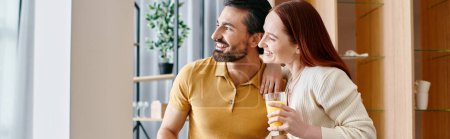 Foto de Una hermosa pareja de adultos, una mujer pelirroja y un hombre barbudo, sonriéndose en su moderna sala de estar. - Imagen libre de derechos