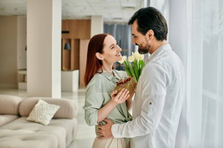 Photo for A stylish adult couple, a redhead woman and a bearded man, holding flowers in a modern living room. - Royalty Free Image