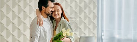 Photo for A redhead woman and bearded man embrace lovingly in front of a chic wall in their modern apartment. - Royalty Free Image