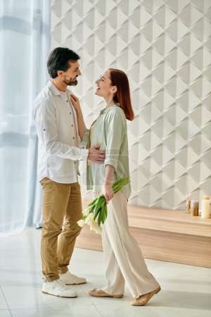 A bearded man and a redhead woman stand together in a modern apartment, exuding love and connection.