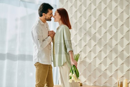 Photo for A redheaded woman and a bearded man standing in front of a wall adorned with vibrant flowers, sharing a moment of connection. - Royalty Free Image
