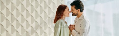Téléchargez les photos : Un couple, une rousse et un barbu s'embrassant devant un mur blanc dans un appartement moderne. - en image libre de droit