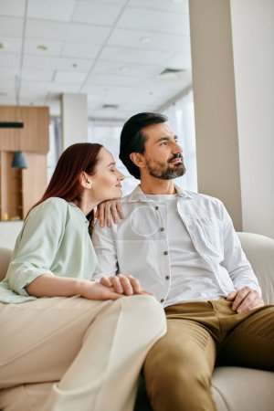 Una hermosa pareja de adultos, una mujer pelirroja y un hombre barbudo, se sientan en un sofá en una sala de estar moderna, pasando tiempo de calidad juntos.