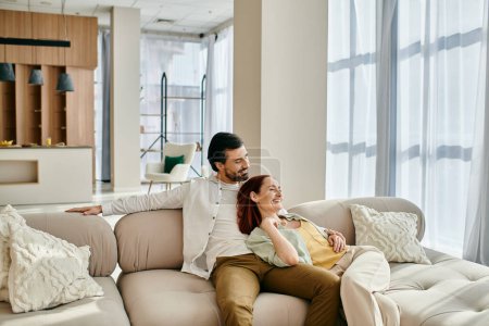 Foto de Un hombre y una mujer, una pelirroja y un hombre barbudo, relajarse en un sofá en una sala de estar moderna, disfrutando de un tiempo de calidad juntos. - Imagen libre de derechos