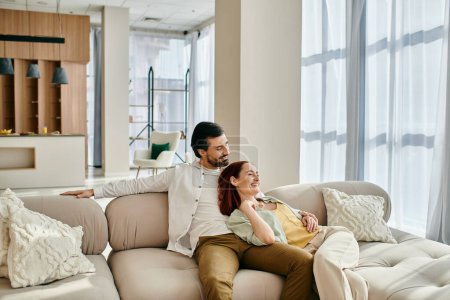 Foto de Un hombre y una mujer, una pelirroja y un hombre barbudo, relajarse en un sofá en una sala de estar moderna, disfrutando de un tiempo de calidad juntos. - Imagen libre de derechos