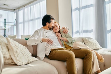 Téléchargez les photos : Une femme rousse et un homme barbu assis sur un canapé confortable, partageant un moment de paix et de connexion dans leur salon moderne. - en image libre de droit
