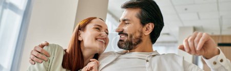Photo for A redhead woman and bearded man hugging warmly in an office setting, showing care and affection - Royalty Free Image