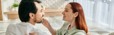 Téléchargez les photos : A redhead woman and bearded man share a tender moment as they gaze into each others eyes in a modern apartment. - en image libre de droit