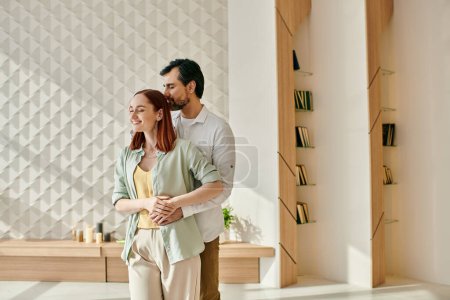 A redheaded woman and bearded man stand in a modern living room, enjoying each others company and the stylish decor.