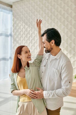Téléchargez les photos : A bearded man and a redhead woman dancing gracefully in a modern apartments living room. - en image libre de droit