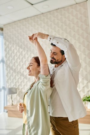 Ein bärtiger Mann und eine rothaarige Frau tanzen fröhlich in einem Büroambiente und bringen Leben und Energie in den Arbeitsplatz.