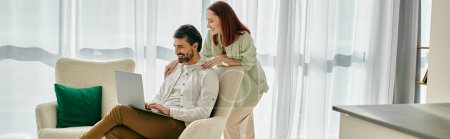 Téléchargez les photos : Une femme rousse et un homme barbu assis sur un canapé, absorbés par l'utilisation d'un ordinateur portable ensemble dans leur appartement élégant. - en image libre de droit