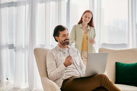 Téléchargez les photos : Une femme rousse et un homme barbu assis sur un canapé, en utilisant un ordinateur portable ensemble dans un appartement moderne. - en image libre de droit