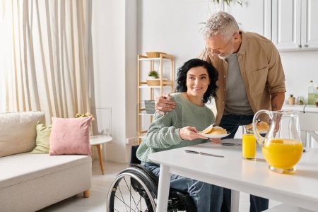 Un homme en fauteuil roulant nourrit amoureusement sa femme handicapée un morceau de nourriture dans leur cuisine.