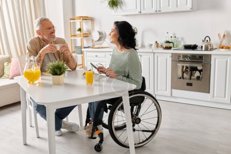 A man in a wheelchair engaged in conversation with a woman in a wheelchair in a cozy kitchen setting at home.