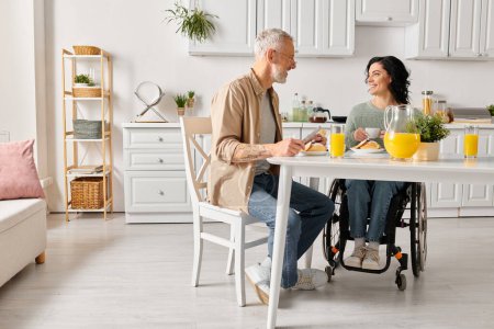 Una mujer discapacitada en silla de ruedas y su marido compartiendo un momento tranquilo en la mesa de su cocina en casa.
