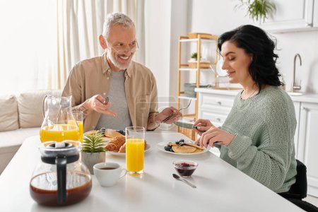 Téléchargez les photos : Un homme et une femme handicapée en fauteuil roulant partagent un repas à leur table de cuisine, profitant d'un petit déjeuner paisible ensemble. - en image libre de droit