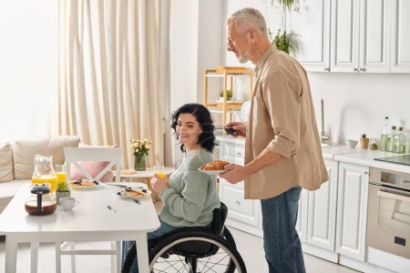 Foto de Una mujer discapacitada en silla de ruedas y su marido preparando una comida juntos en su cocina en casa. - Imagen libre de derechos