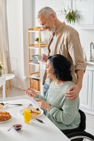 Foto de Una pareja casada, el marido y la esposa discapacitada, comparten una comida juntos en una mesa de la cocina en su casa. - Imagen libre de derechos