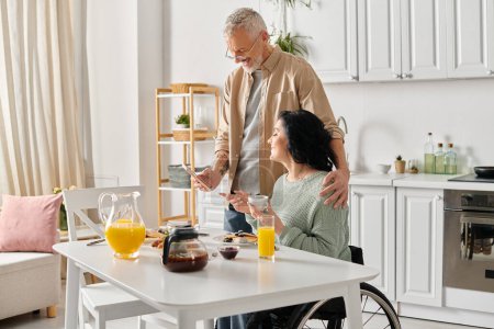A husband stands by his disabled wife in a wheelchair, offering support and companionship in their home kitchen.