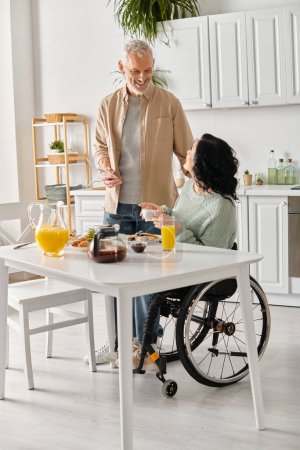 A woman in a wheelchair engaging in conversation with a husband in a kitchen at home.
