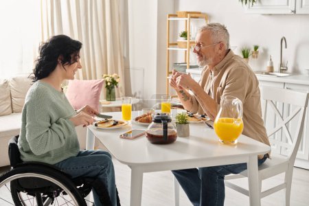 A disabled woman in a wheelchair and her husband share a cozy breakfast in their home kitchen.