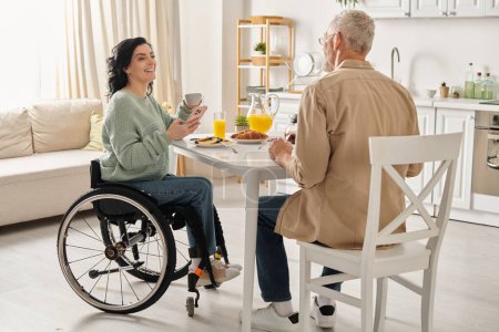 Une femme handicapée en fauteuil roulant et son mari s'assoient ensemble à une table dans une chambre confortable.