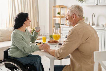 Eine behinderte Frau im Rollstuhl genießt einen Moment mit ihrem Mann an einem Küchentisch in ihrem Haus.