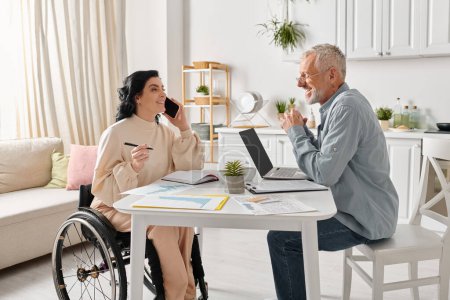 A woman in a wheelchair engages in conversation on phone near man at a table in a cozy kitchen setting.