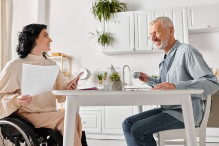 A man in a wheelchair engages in conversation with a woman in a kitchen at home.