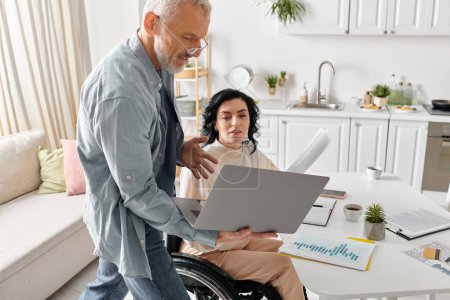 Eine Frau im Rollstuhl mit einem Laptop in einer gemütlichen häuslichen Umgebung, in der Nähe ihres Mannes