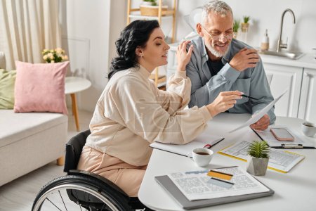 Photo for A man and a wheelchair-bound woman planning family budget together at their kitchen table at home. - Royalty Free Image